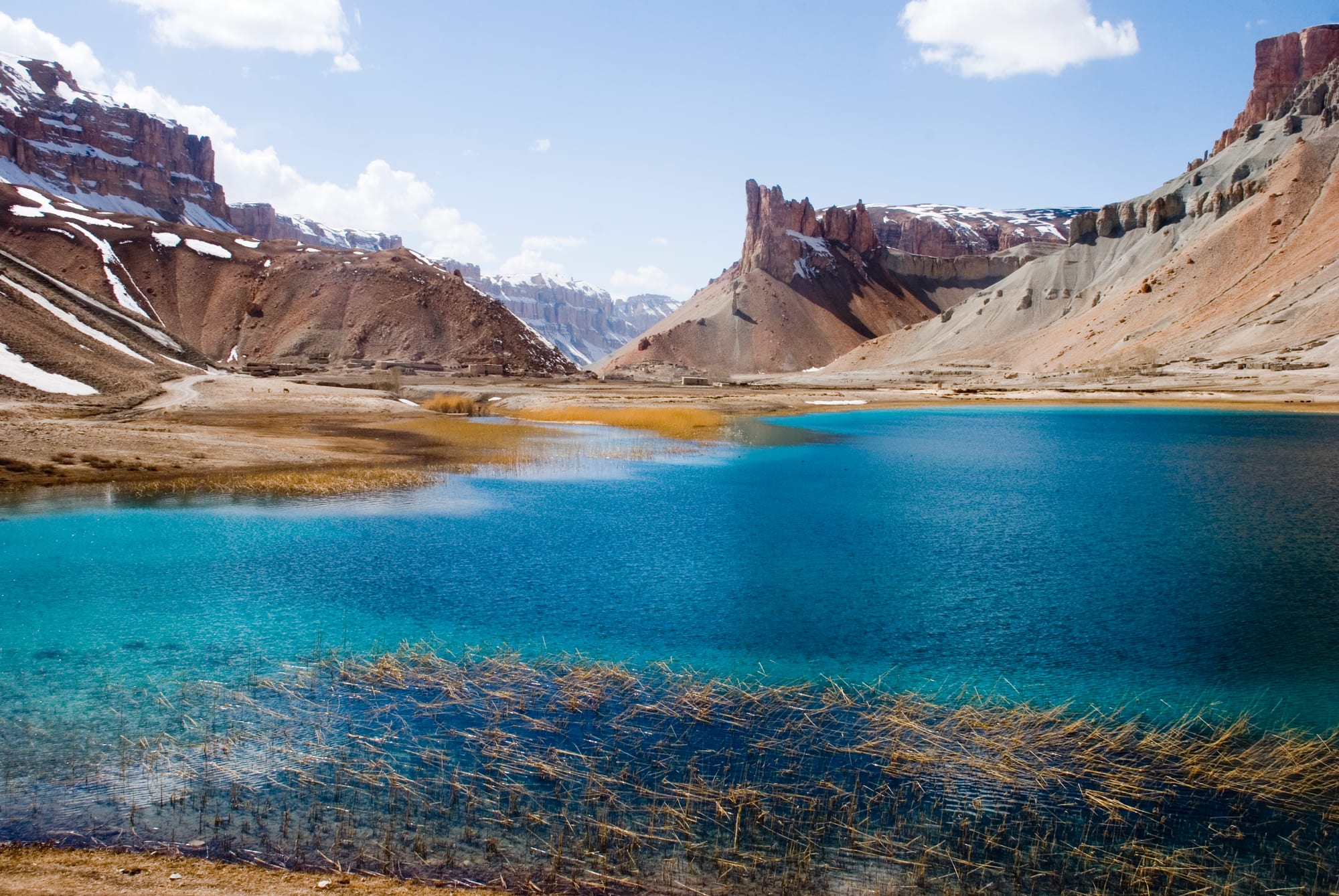 A bright turquoise lake ringed by snow and bare desert hills