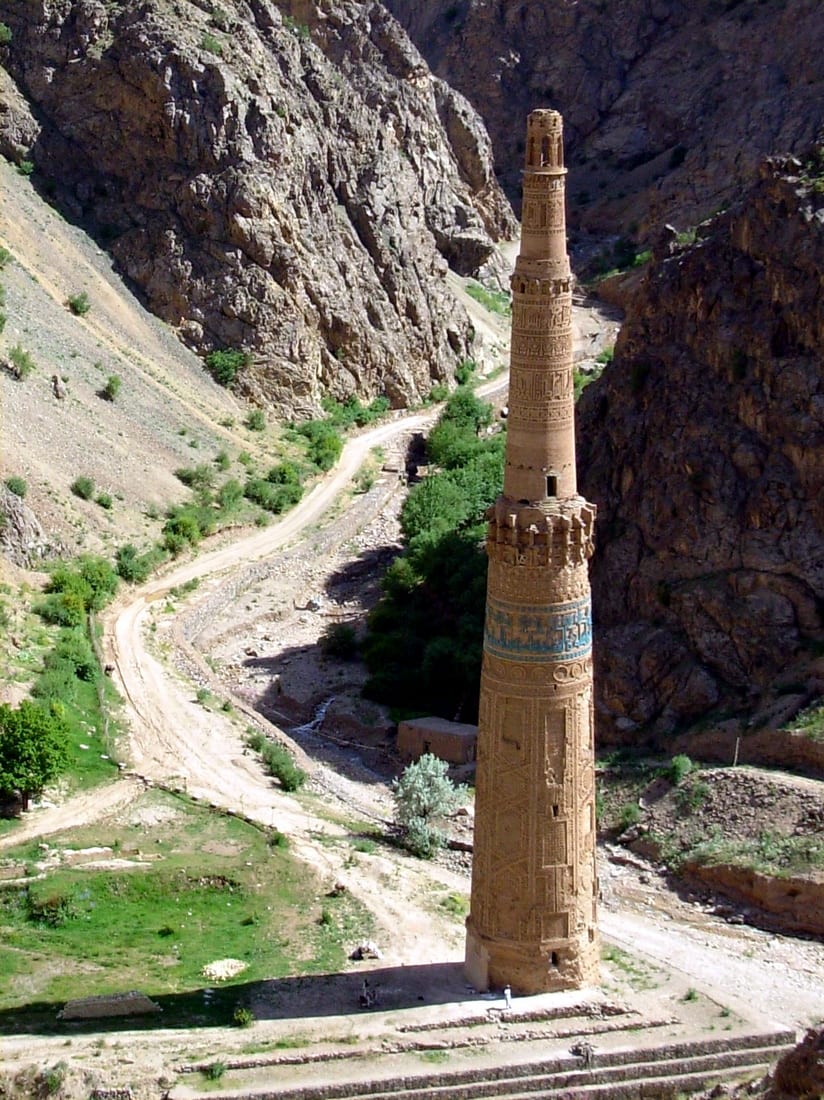 A tall, slender, richly decorated brick tower standing alone in a bare mountain gorge