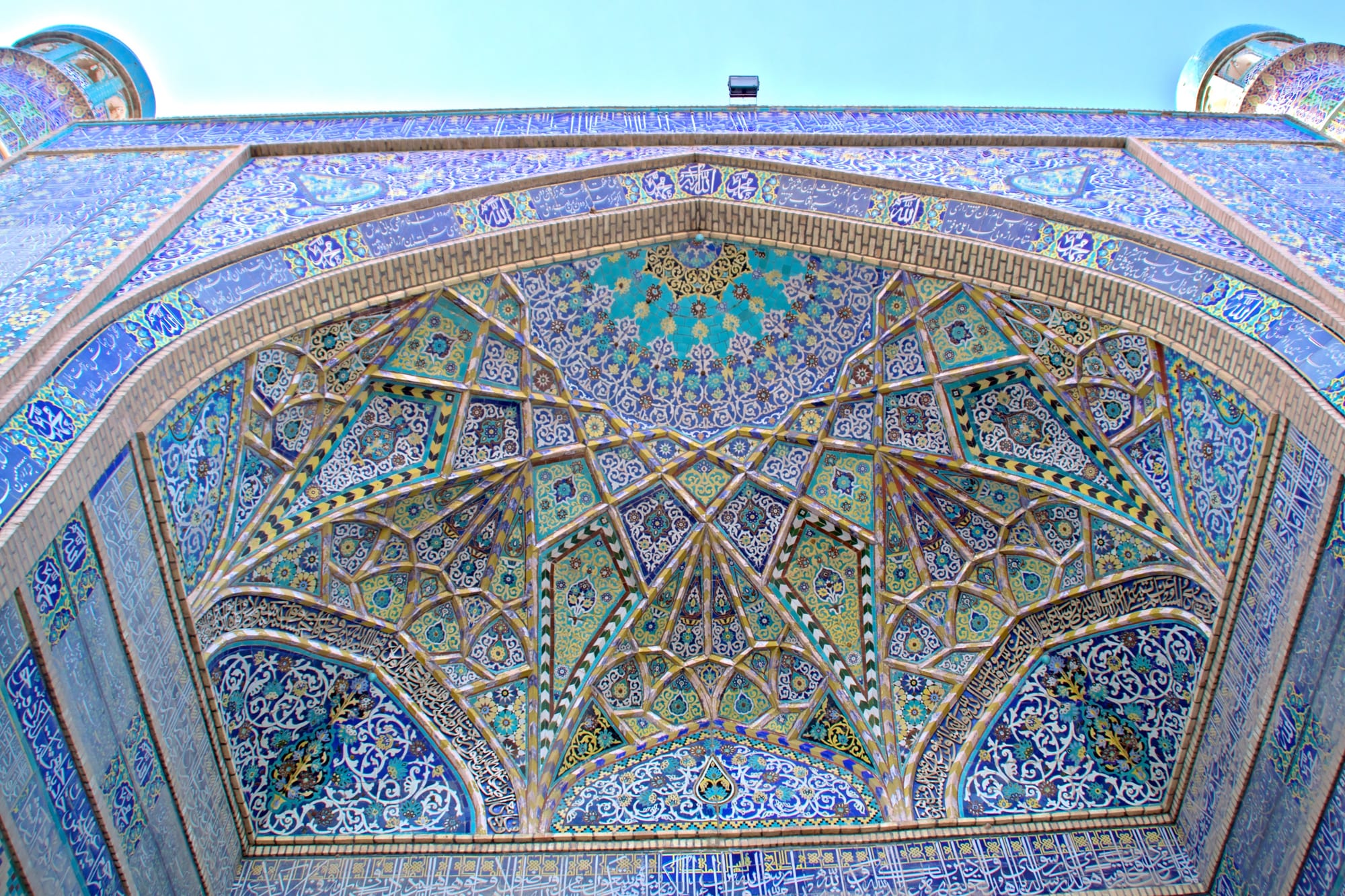 A grand tiled entrance portal and courtyard of a historic mosque, every surface covered in blue mosaic