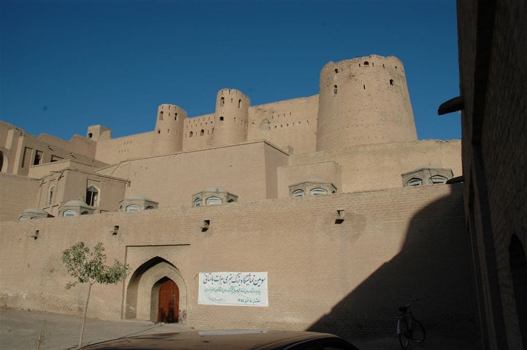 A large restored mud-brick fortress with round towers standing on a low rise above a city