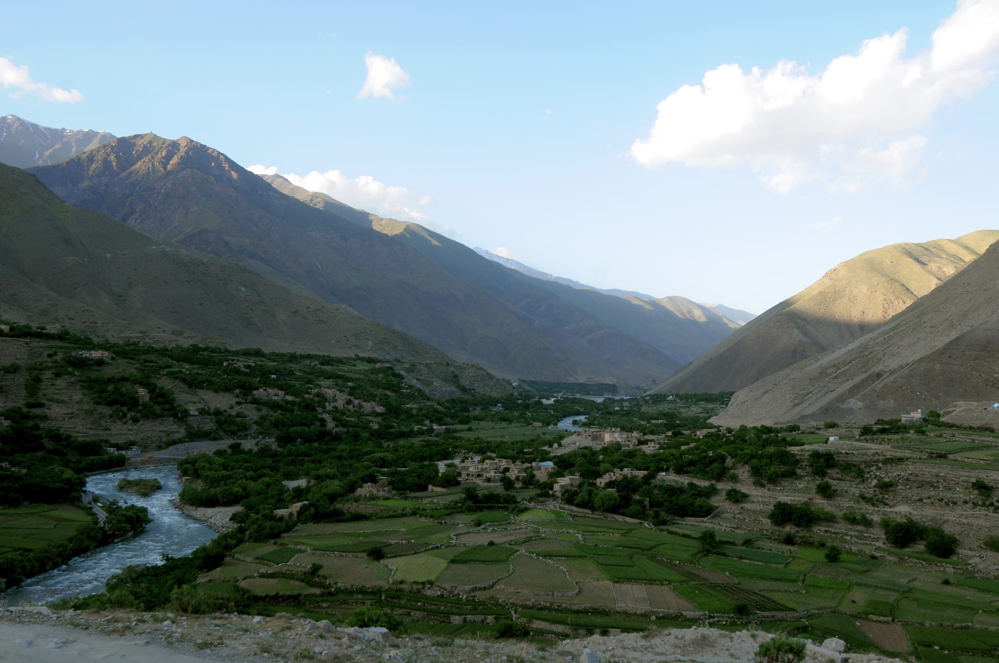 A green river valley with terraced fields winding between steep, dry mountain walls