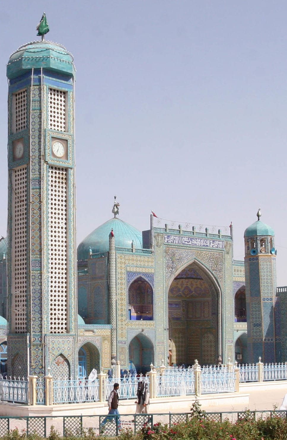 A large mosque covered in blue and turquoise tilework under a clear sky, with pigeons in the courtyard