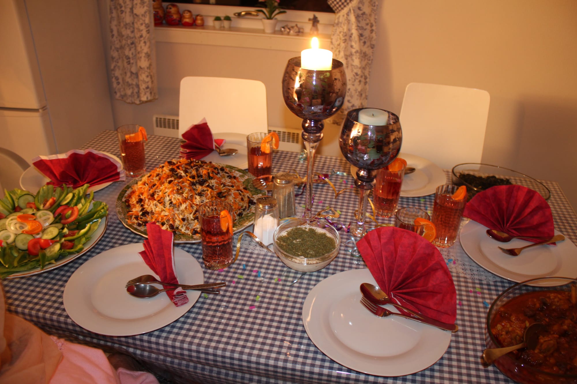 A large oval platter of brown rice topped with orange shredded carrot and dark raisins, on a laid table with a salad plate, a bowl of green chutney and glasses of tea