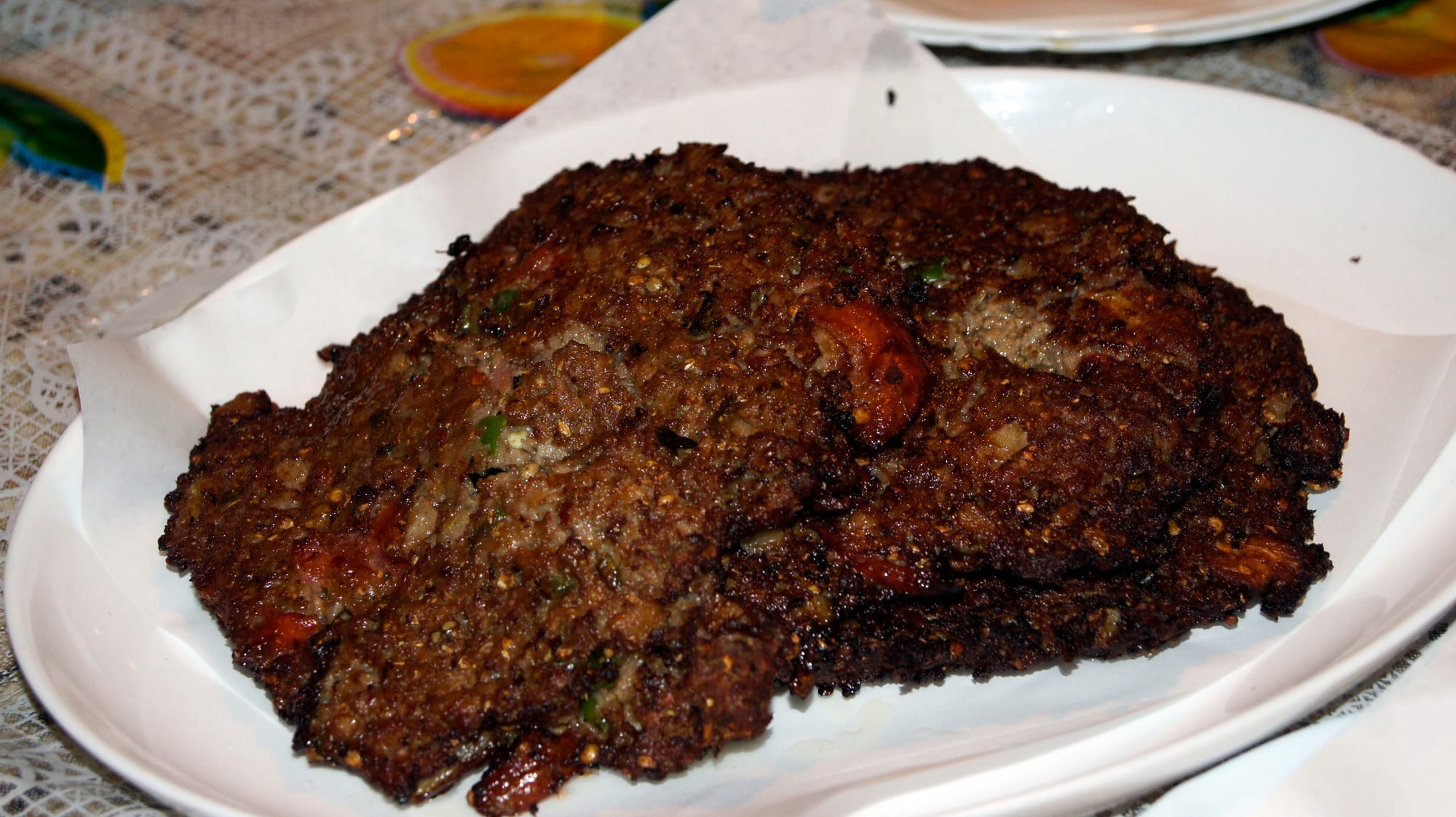 Two large thin dark-brown fried minced-meat patties with ragged edges on a paper-lined plate
