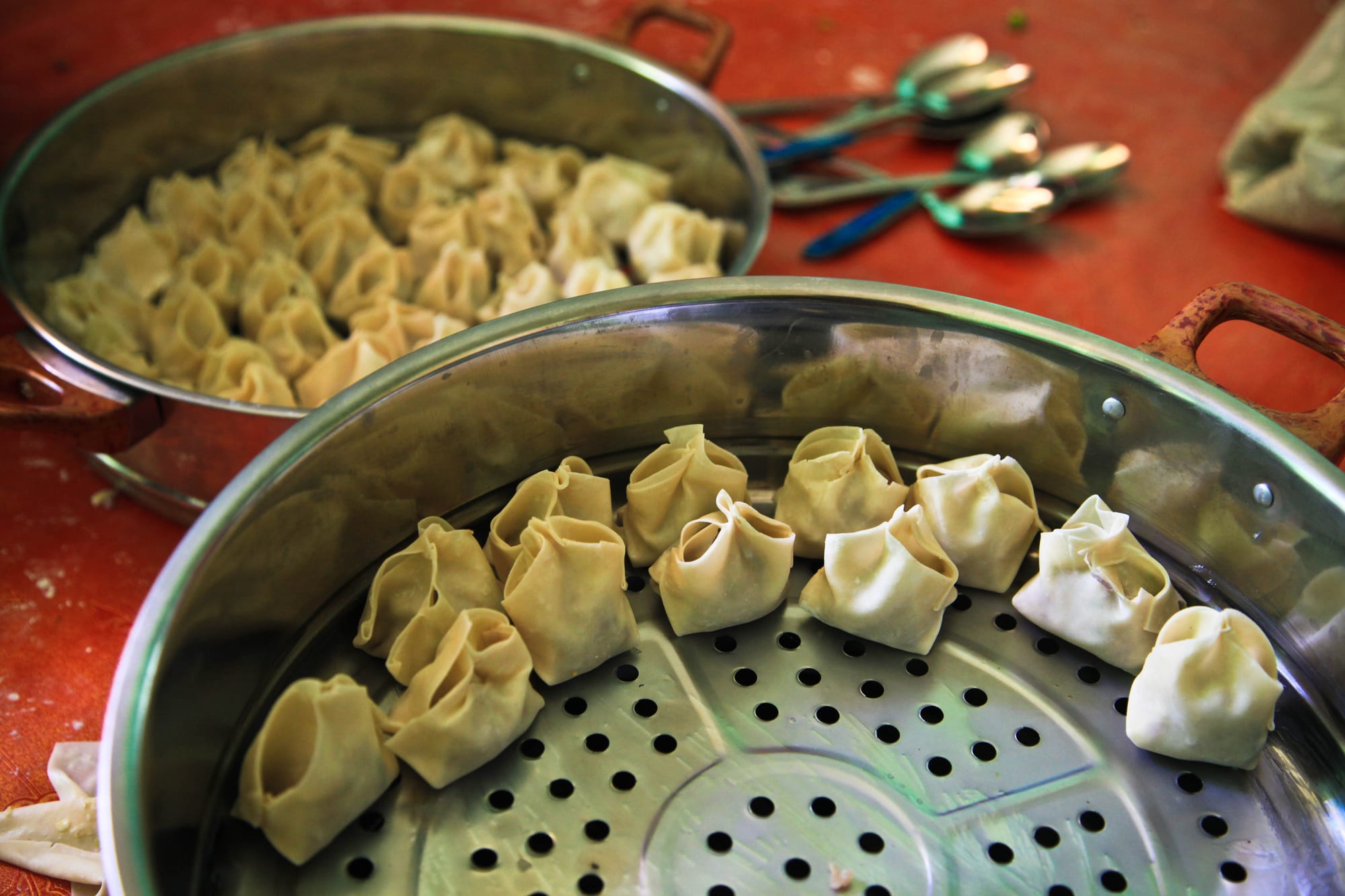 Two round metal steamer trays holding rows of small folded dough dumplings