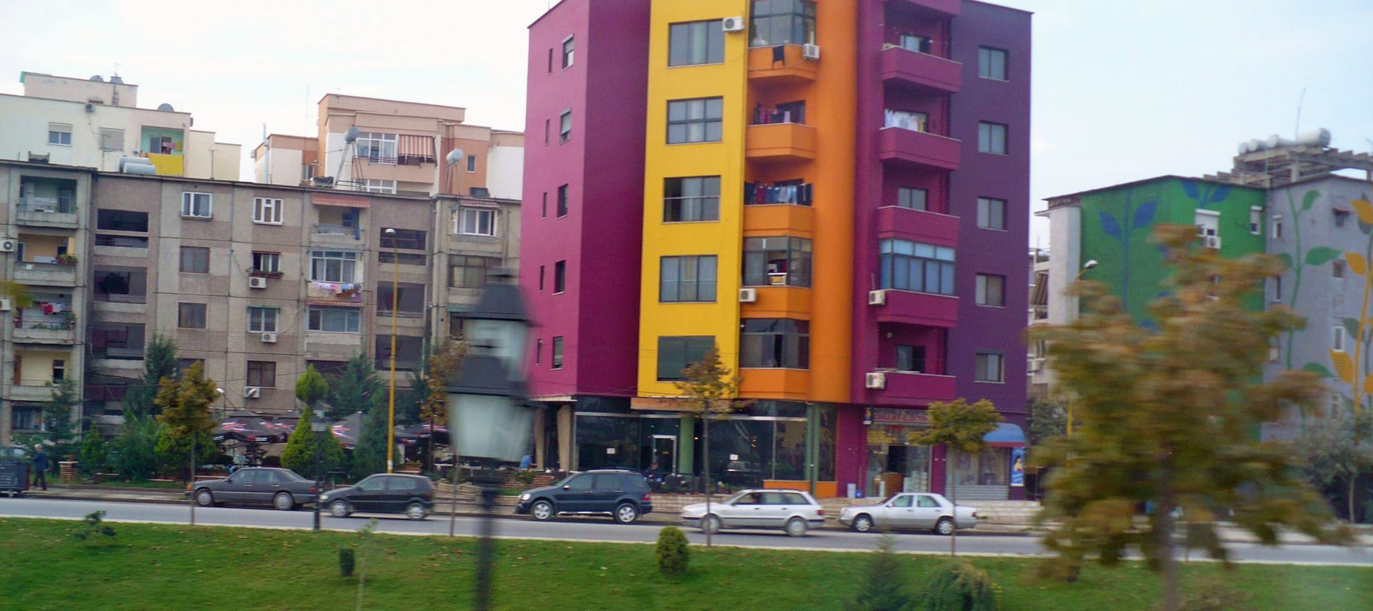 Rows of Tirana apartment blocks, some painted in bright pink, yellow, orange and purple, with laundry hanging from balconies