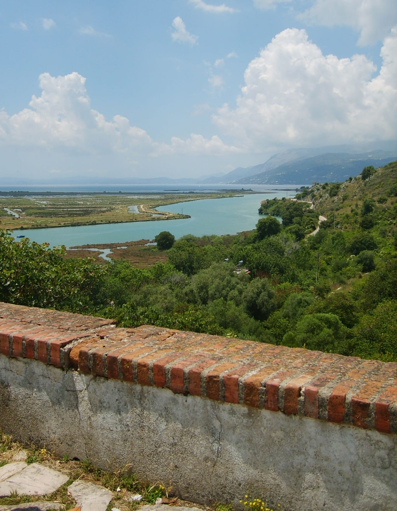 A wooded peninsula with ancient stone ruins beside a calm blue channel, hills beyond