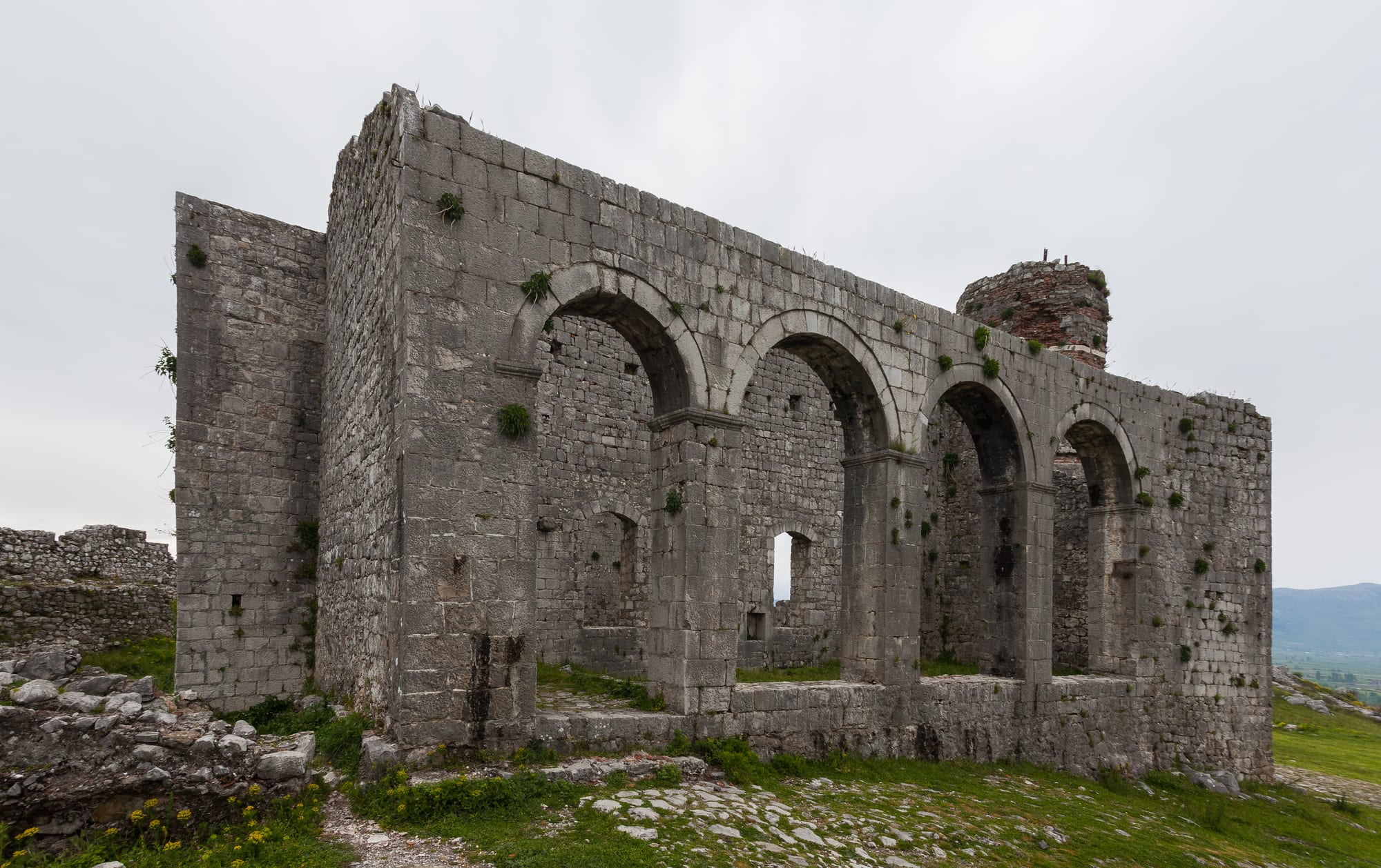Long stone fortress walls on a green hill above a plain, a wide river winding beyond