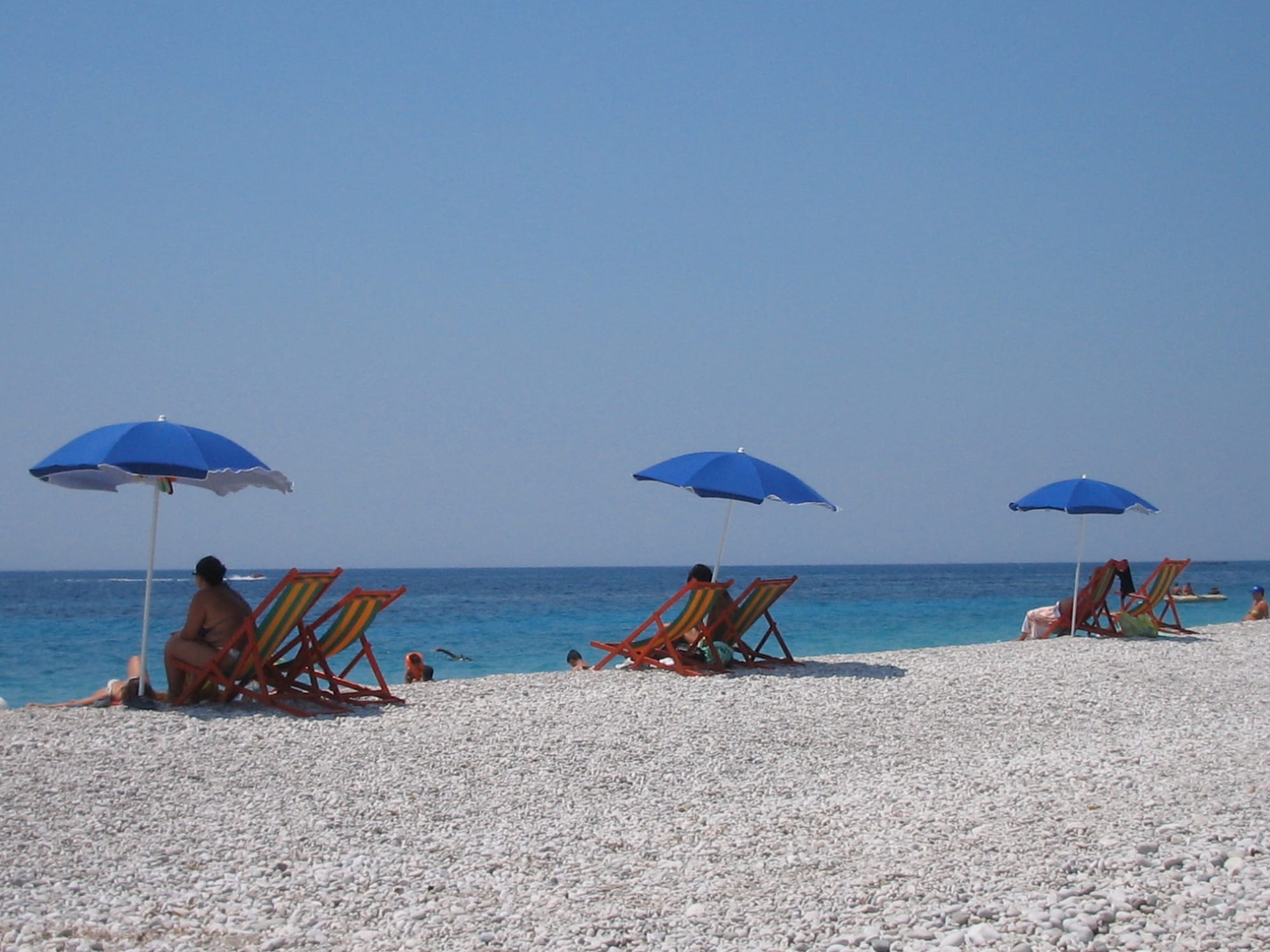 A pebble beach and clear water below steep dry mountains dropping straight to the sea