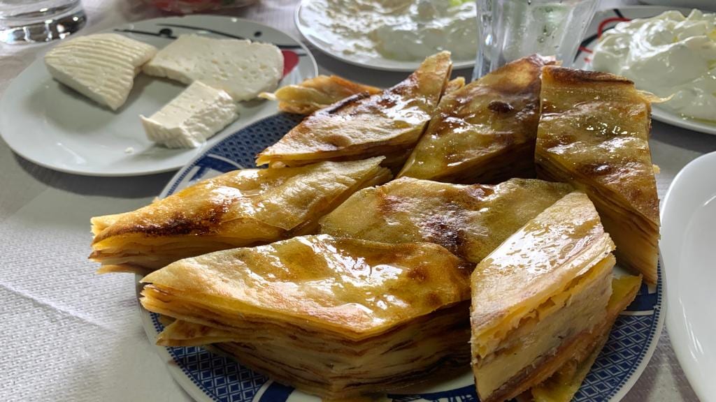 A plate of wedge-cut layered pastry showing many thin baked layers in cross-section, with white cheese and cream on plates alongside