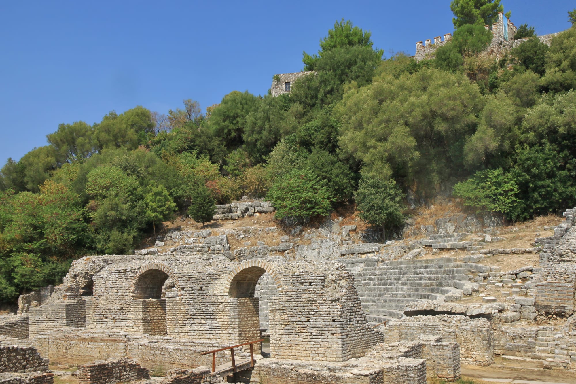 A Greek and Roman stone theatre backed by a medieval fortress tower and ringed by trees