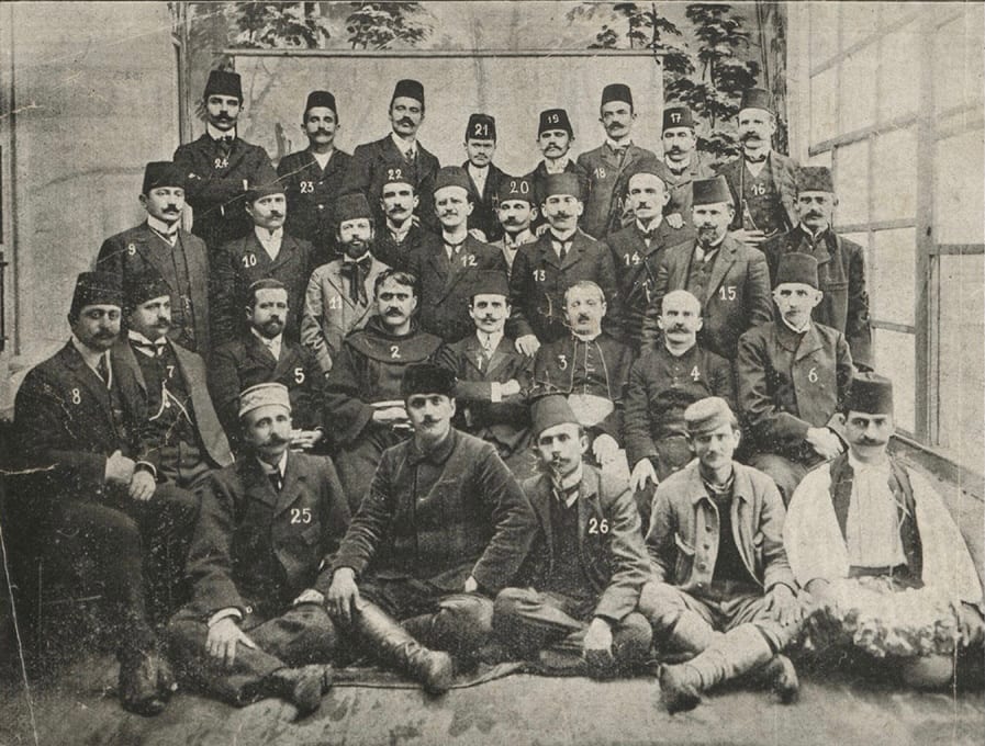 A formal 1908 group photograph of around thirty seated and standing delegates in suits and fezzes