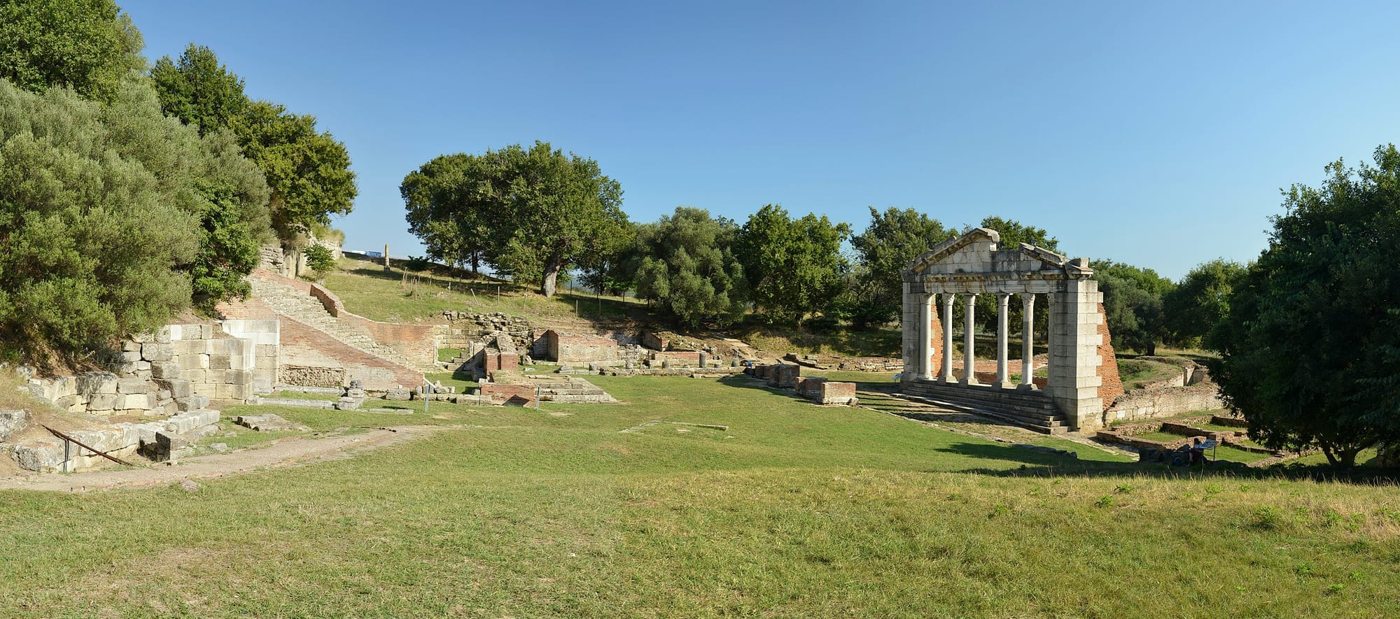 A hillside of excavated Roman ruins with a restored colonnade and open countryside beyond