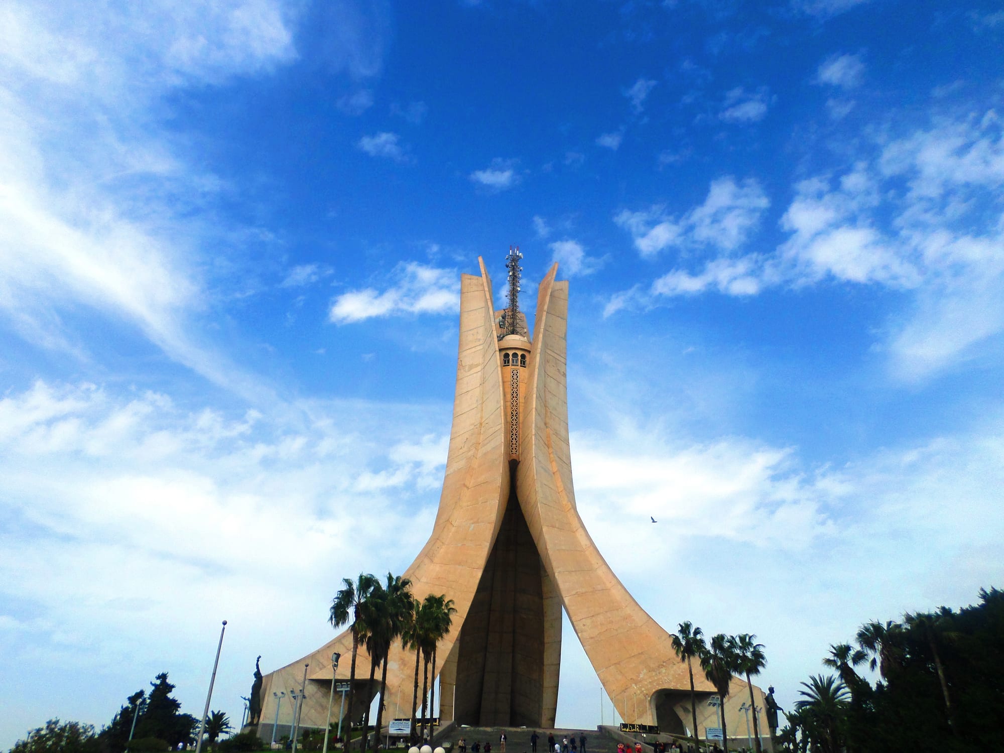 A huge concrete monument of three curved fronds meeting at a peak, over an eternal flame
