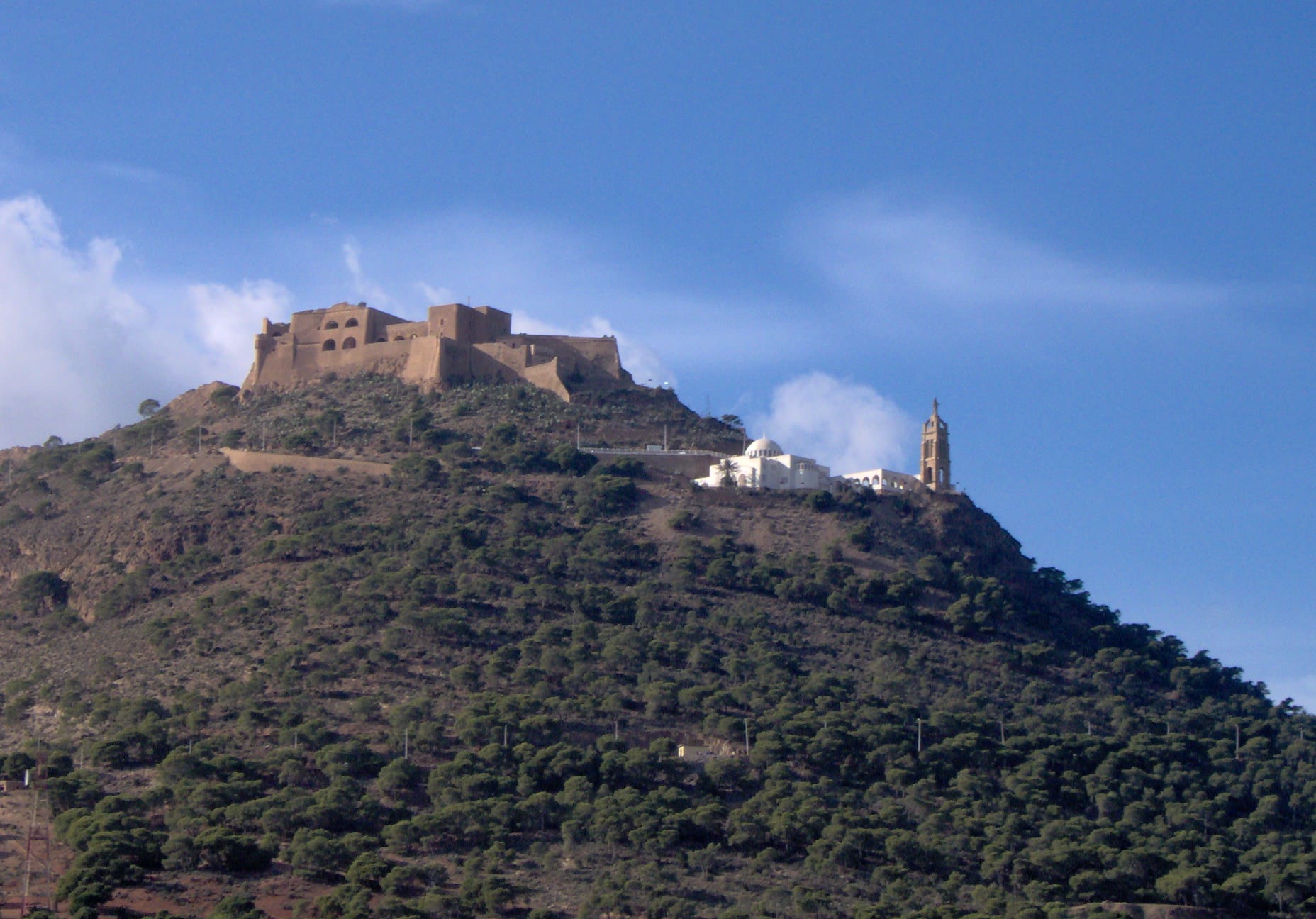 A Spanish fort and chapel on a high coastal cliff above a city and bay