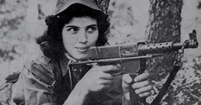A young woman in fatigues with a rifle, photographed in the field during the 1950s