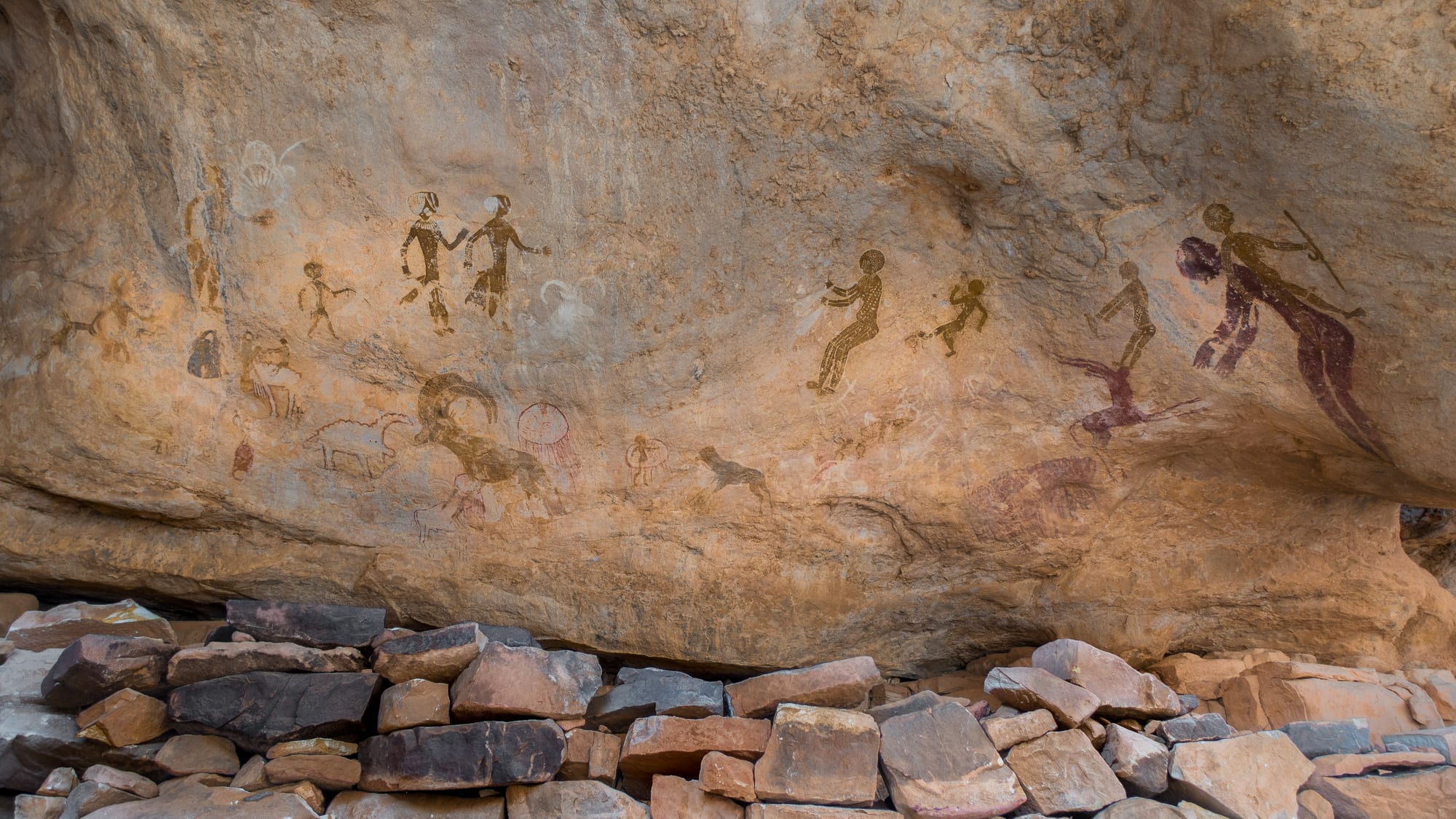 Faded ochre paintings of human figures and animals on a pale rock wall in the desert