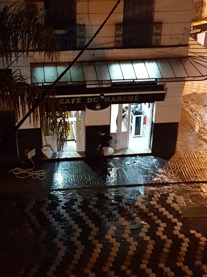 The lit storefront of Café du Marché, a small café in central Algiers, on a wet evening