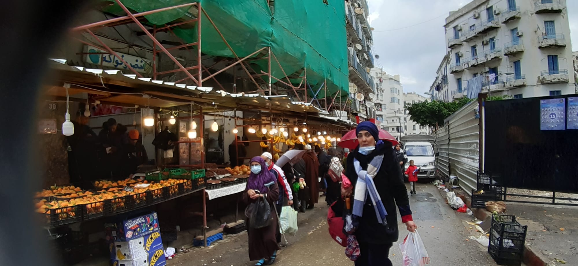 A busy open-air produce market street in the Bab el Oued neighbourhood of Algiers, with shoppers and fruit stalls