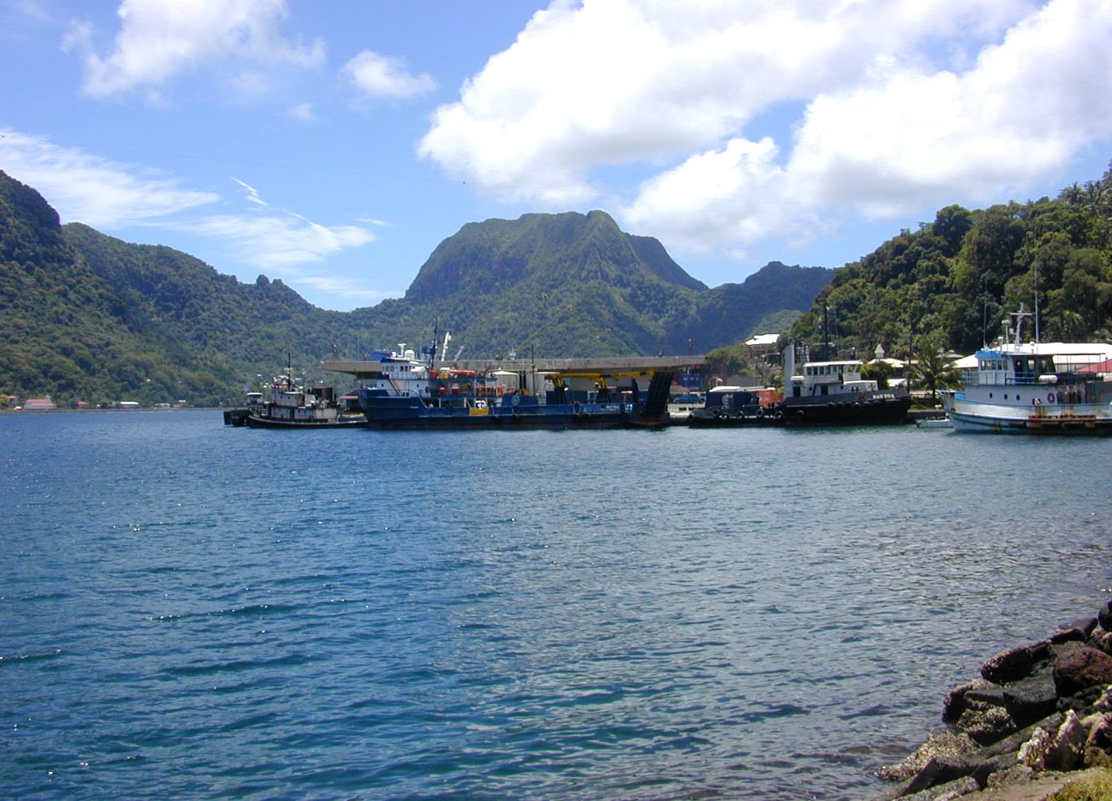 A harbour dock with a sharp green peak rising steeply behind it