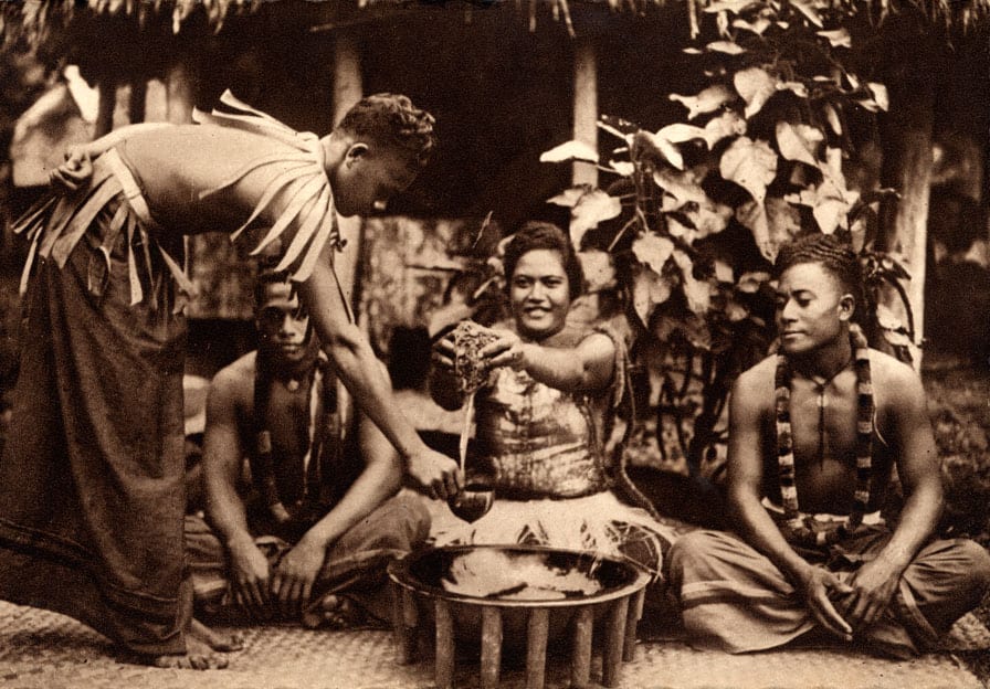 An early 20th-century photograph of men seated on mats around a large low wooden bowl