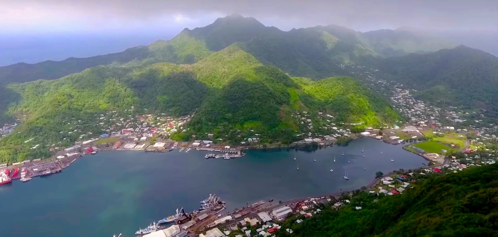 A deep blue harbour ringed by steep green volcanic ridges, with a small town along the shore