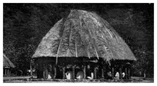 An oval thatched open-sided house on posts, with several men seated cross-legged inside