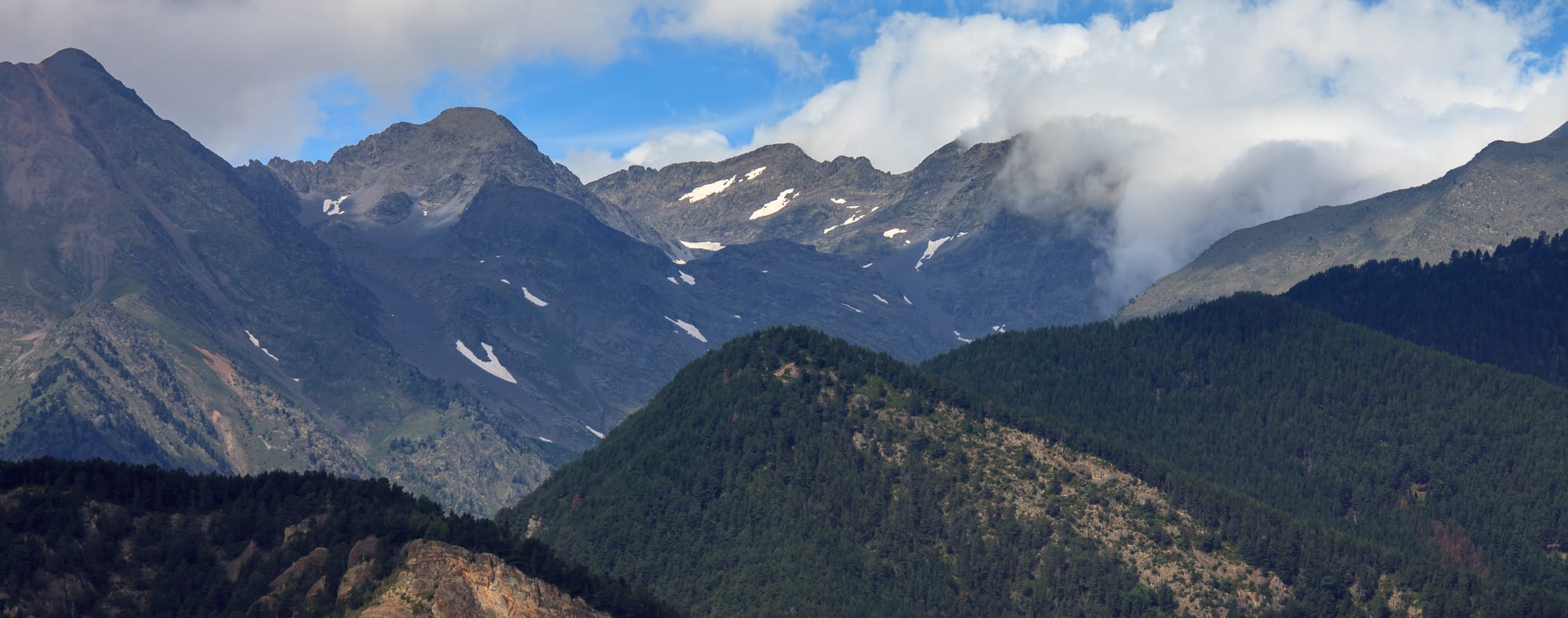 Steep forested and rocky mountains under snow patches, a green valley floor below