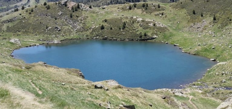 A still mountain lake reflecting bare grey peaks, low scrub around the shore