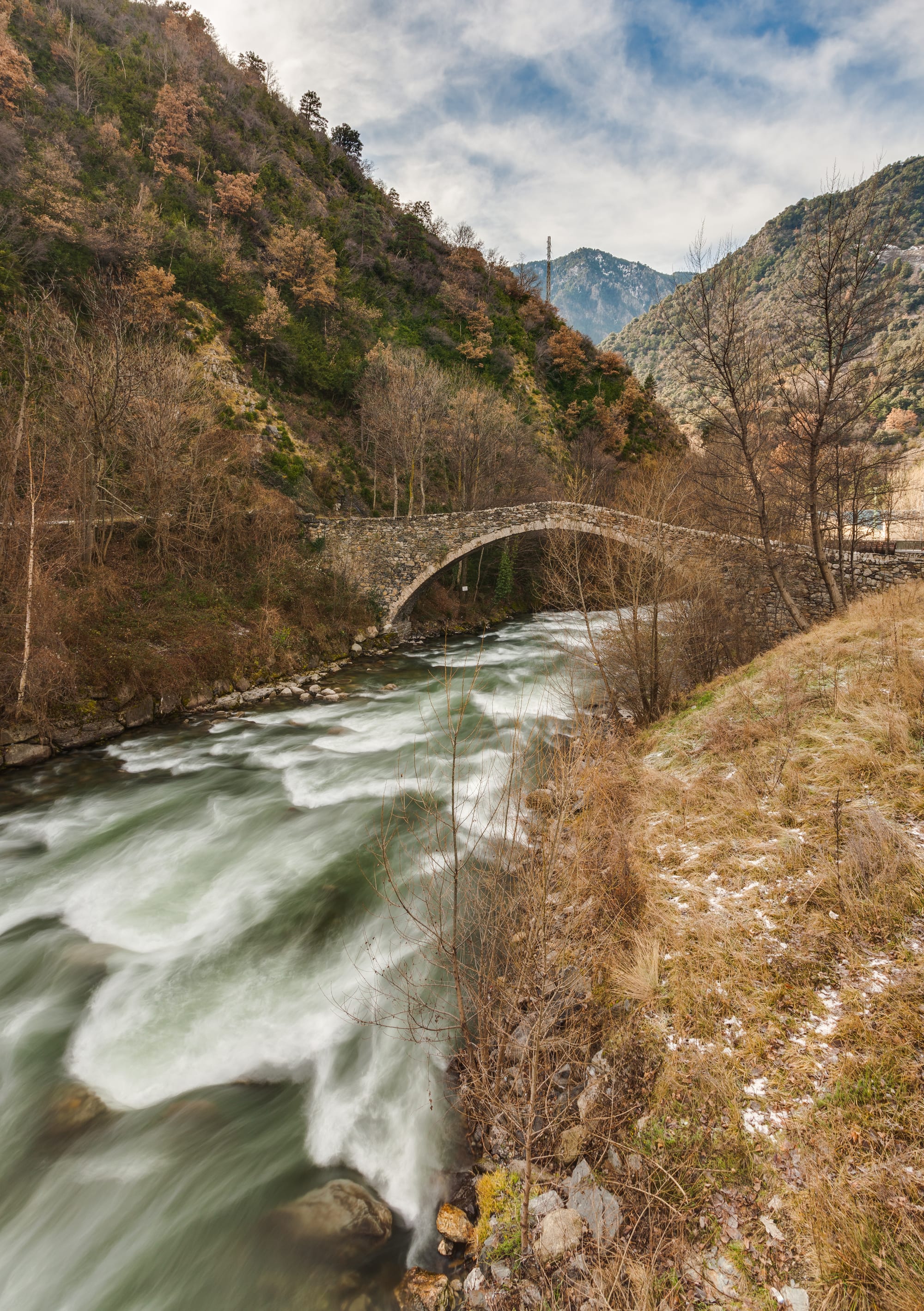 A steep single-arched medieval stone bridge over a river, town buildings behind