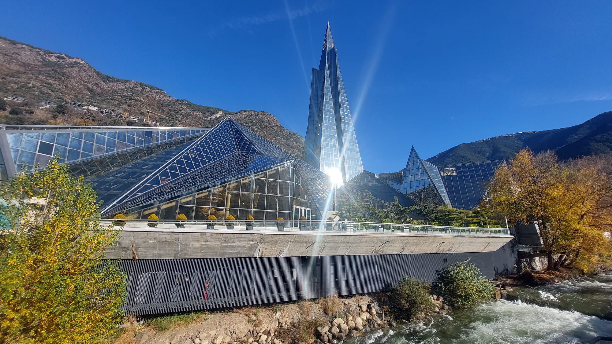 A tall futuristic glass spire rising above a spa complex in a narrow town
