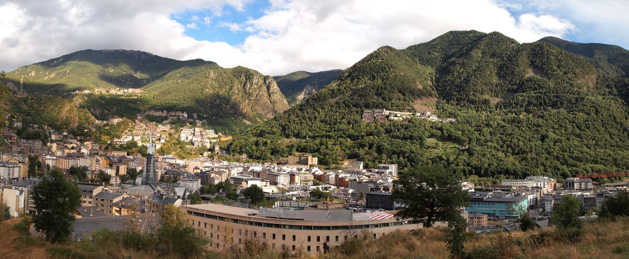 A dense small city of pale apartment blocks filling a narrow valley floor between steep forested mountains