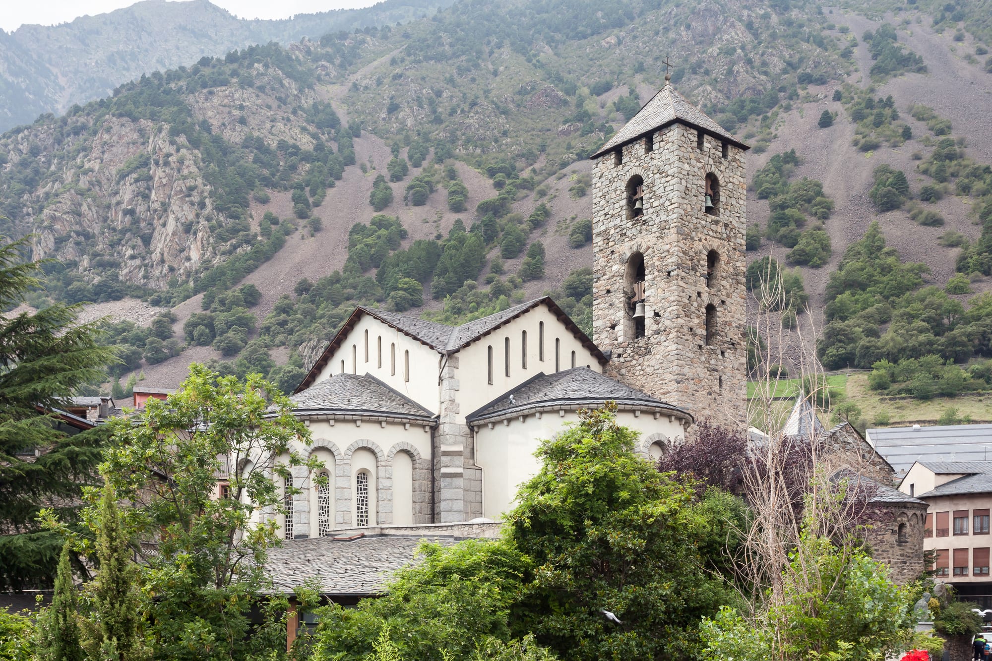 A stone church with a rounded apse and bell tower beside a modern square