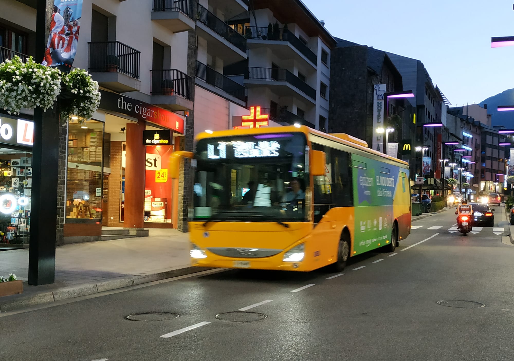 A yellow city bus on route L1 driving through central Andorra la Vella at dusk