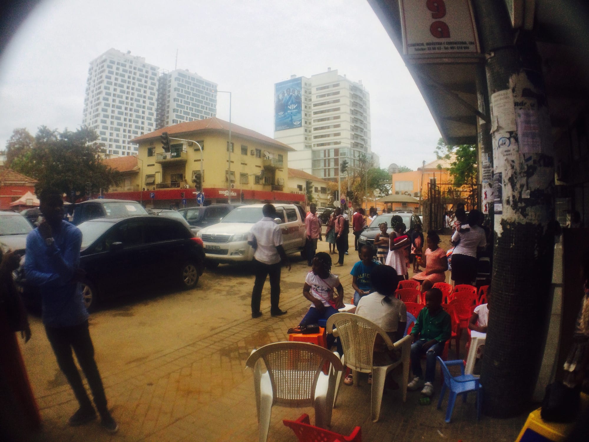 People standing and talking on a street in the Maculusso neighbourhood of Luanda, with a colonial-era building and modern towers behind