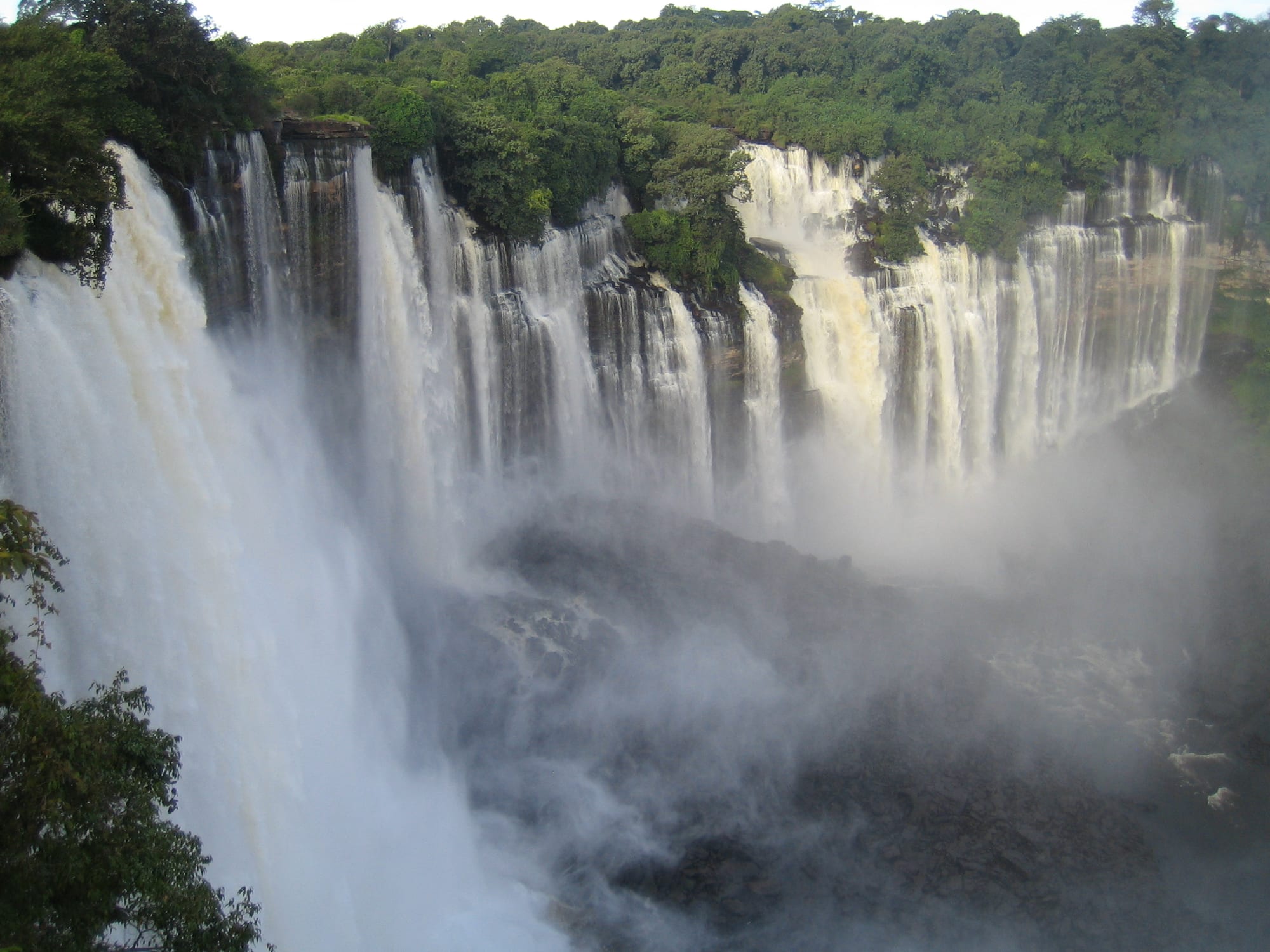 A broad horseshoe waterfall pouring over a green cliff, spray rising from the pool below