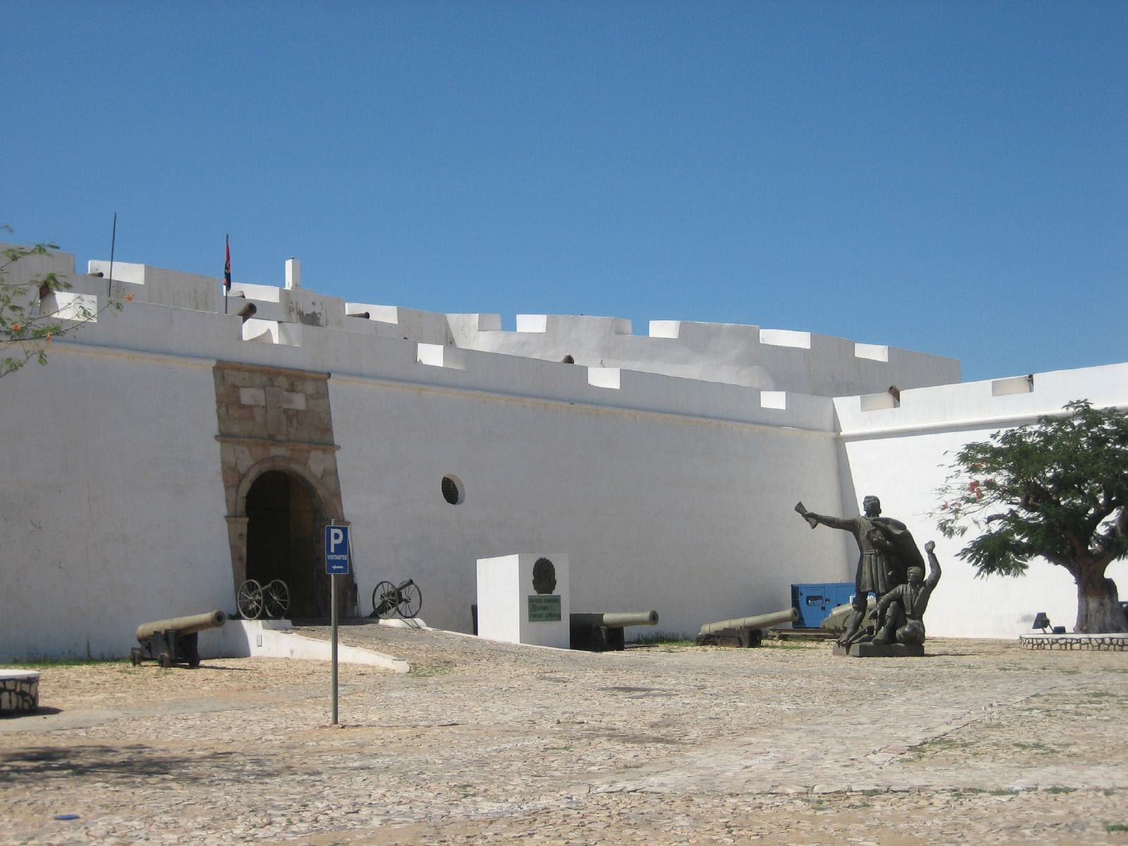 Thick whitewashed fortress walls with cannon on a rise above a harbour
