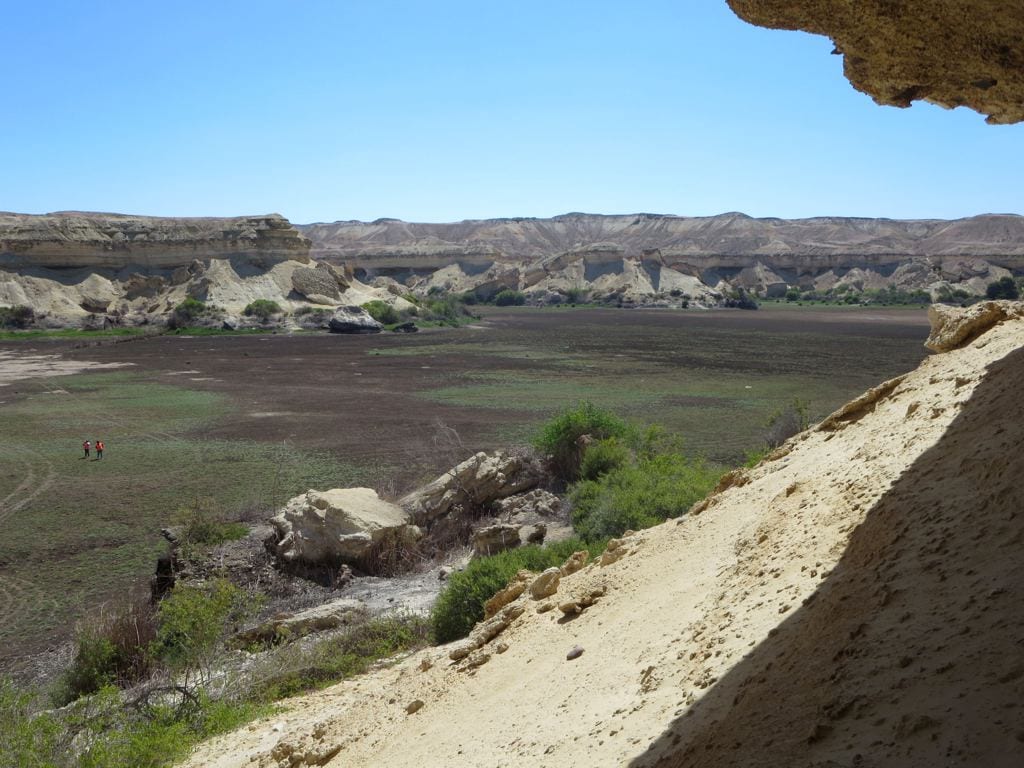 A green reed-fringed lagoon at the foot of red desert cliffs
