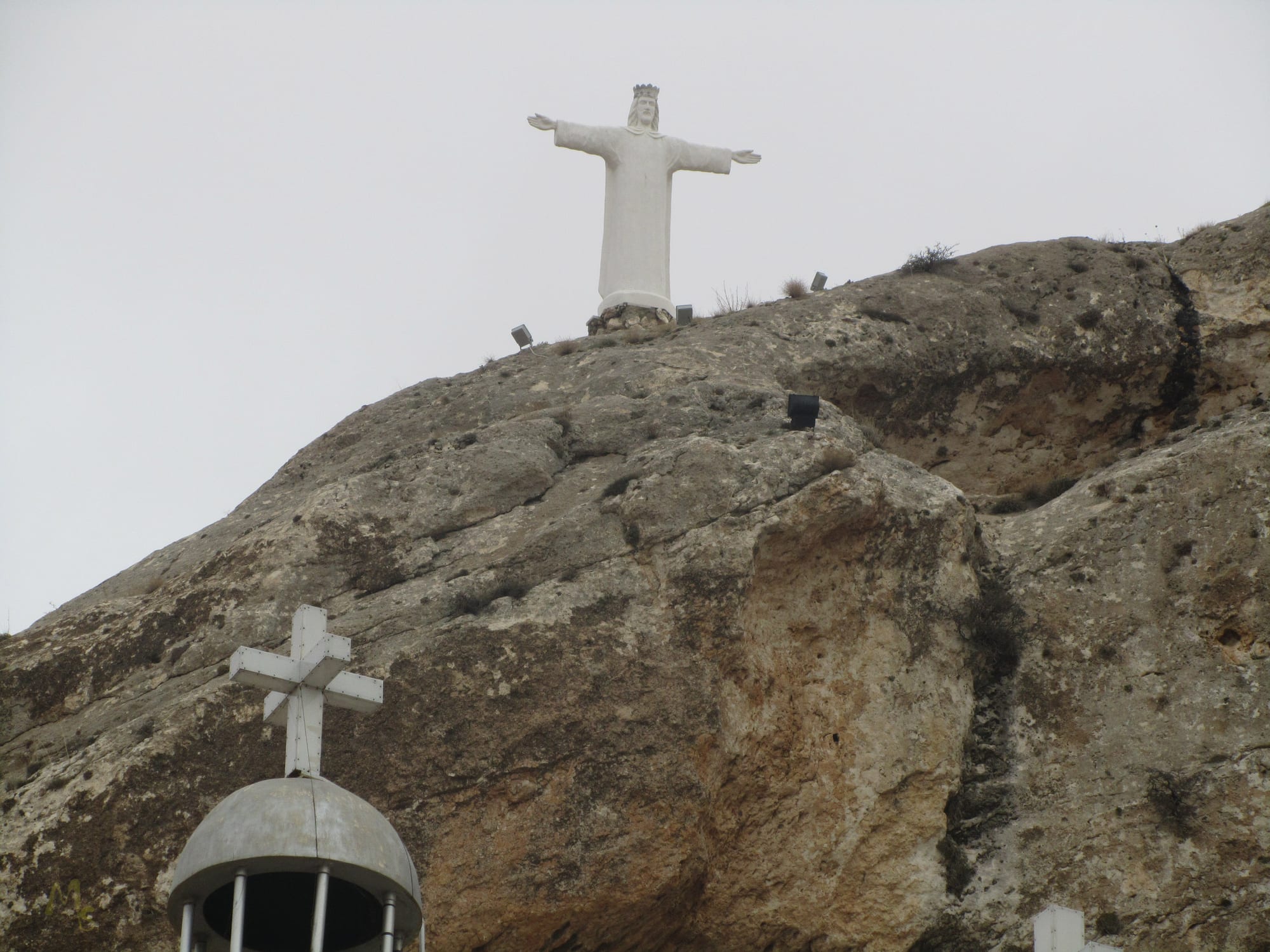A white statue of Christ with arms outstretched on a hilltop above a city