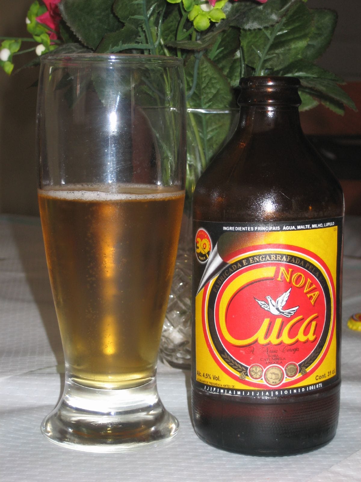 A glass of pale golden beer next to an unopened brown bottle labelled Cuca