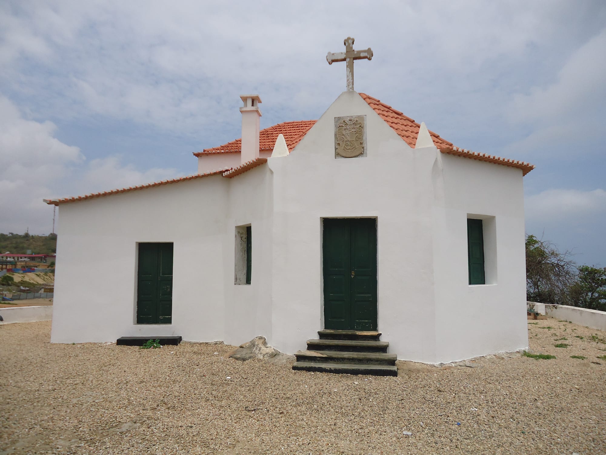 A small whitewashed colonial chapel with a red-tiled roof, near the sea