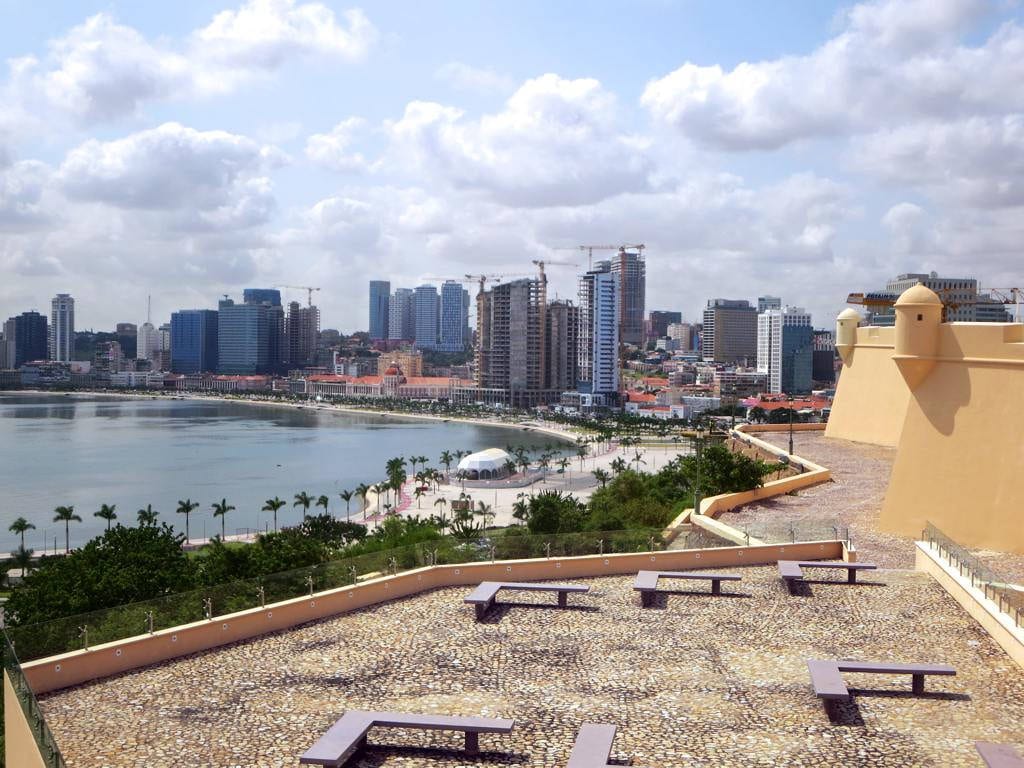 A waterfront row of glass high-rise towers along a curving bay, with older buildings behind