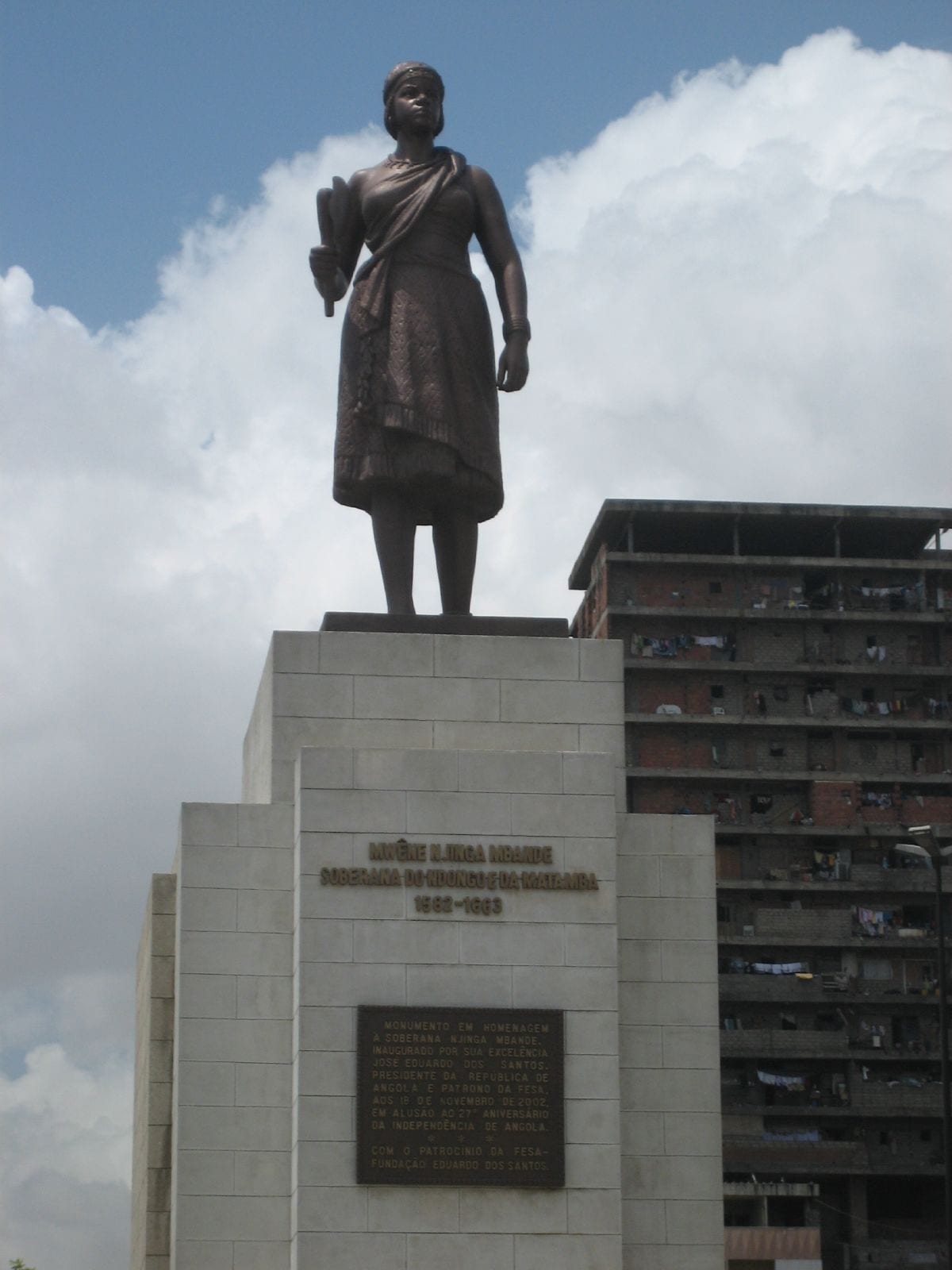 A bronze statue of a standing woman in a wrapped robe and headband, holding an axe, on a tall pale stone plinth