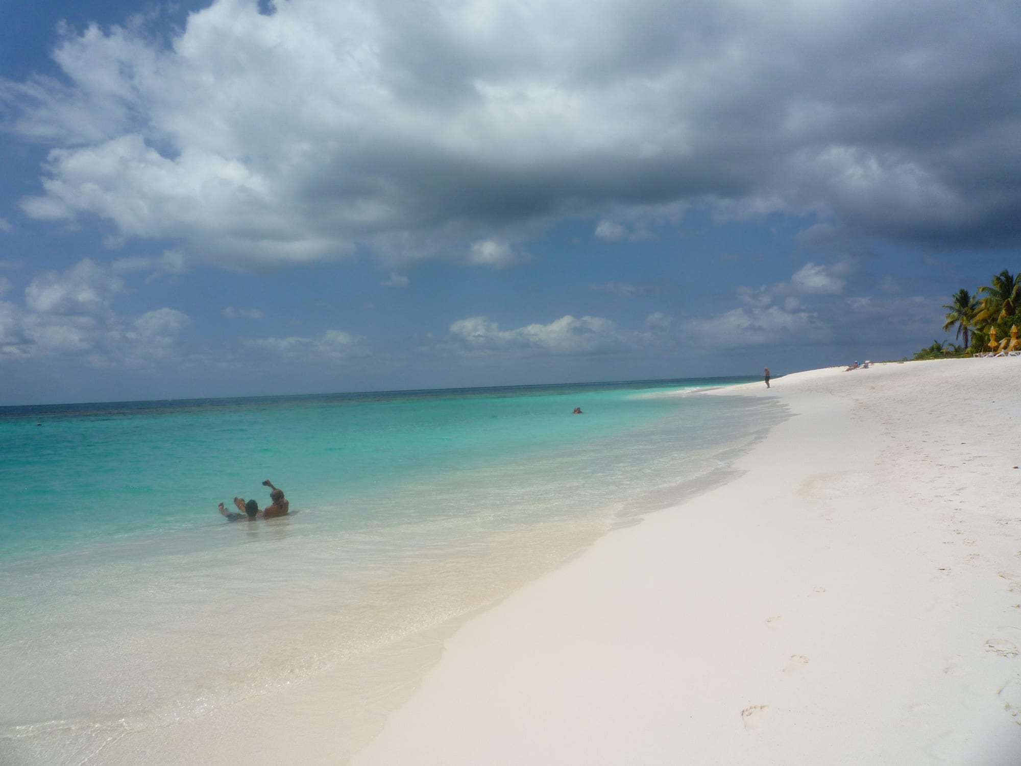 A long curve of bright white sand with calm clear water and a few beach umbrellas
