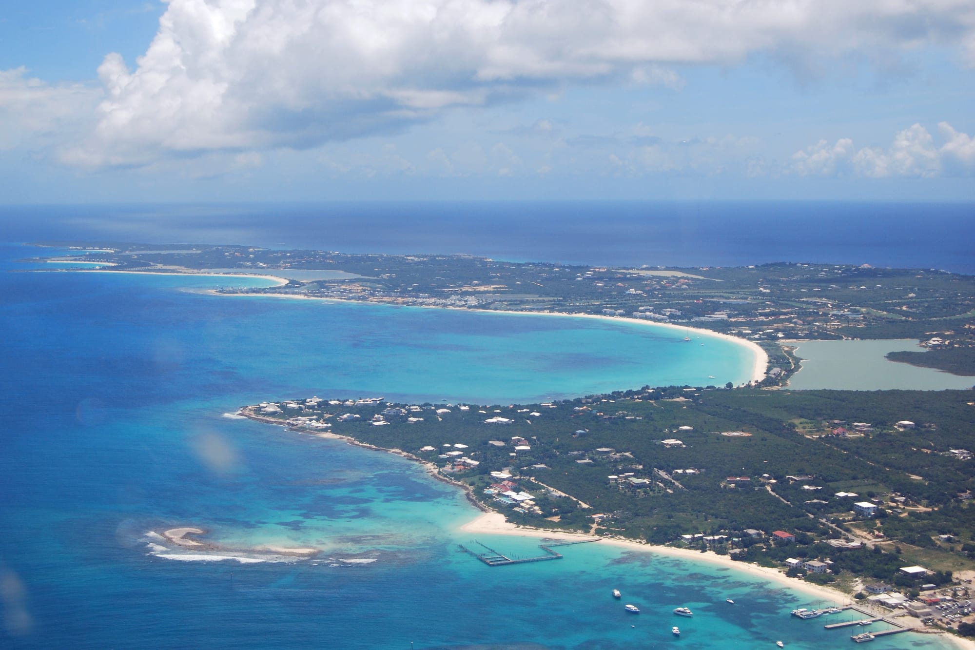 Aerial view of a dry green island end fringed by several white beaches and reefs