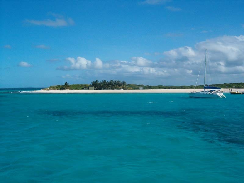 A low uninhabited cay with cliffs at one end and a white beach, clear reef water around