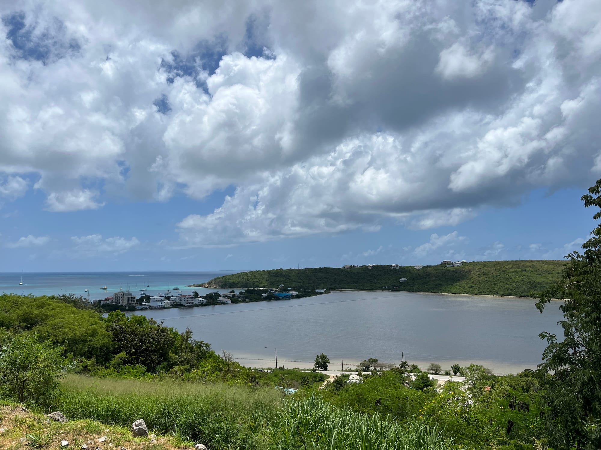A shallow still salt pond behind a beach, ringed by low scrub under a wide sky