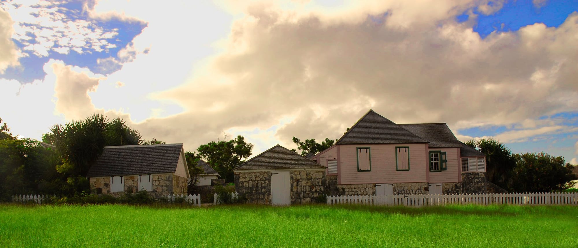A low white 18th-century plantation house with a wide veranda and green shutters among palms