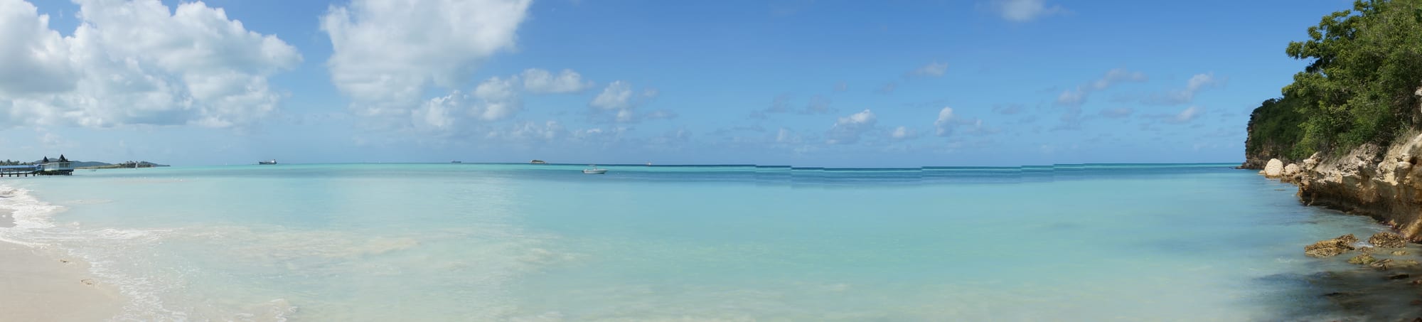 A long calm white beach with resorts set back among palms, flat blue sea