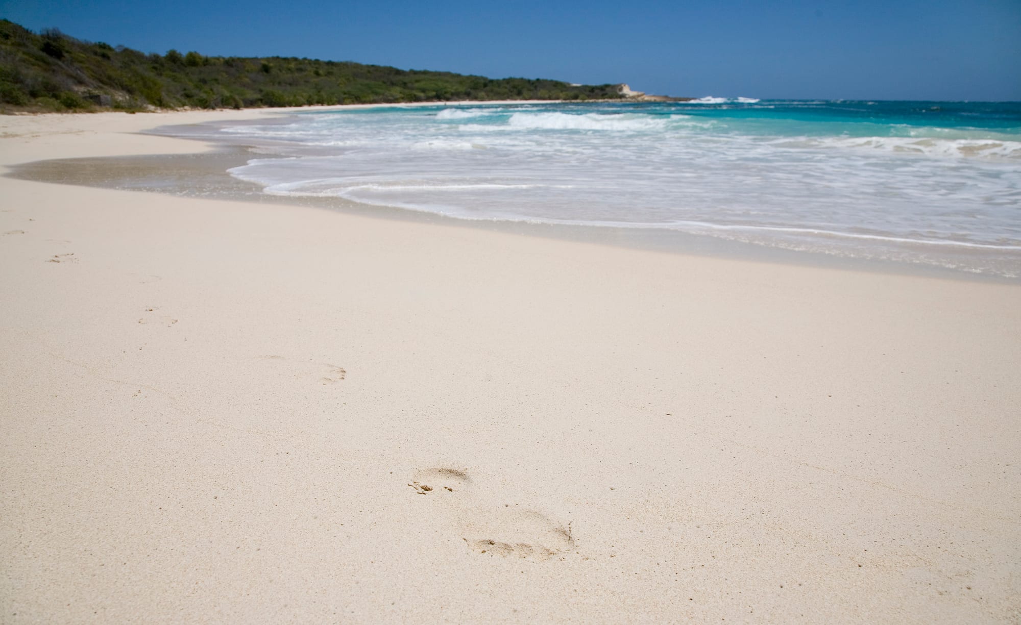 A perfect crescent of pale sand enclosing turquoise water, green headlands at each end